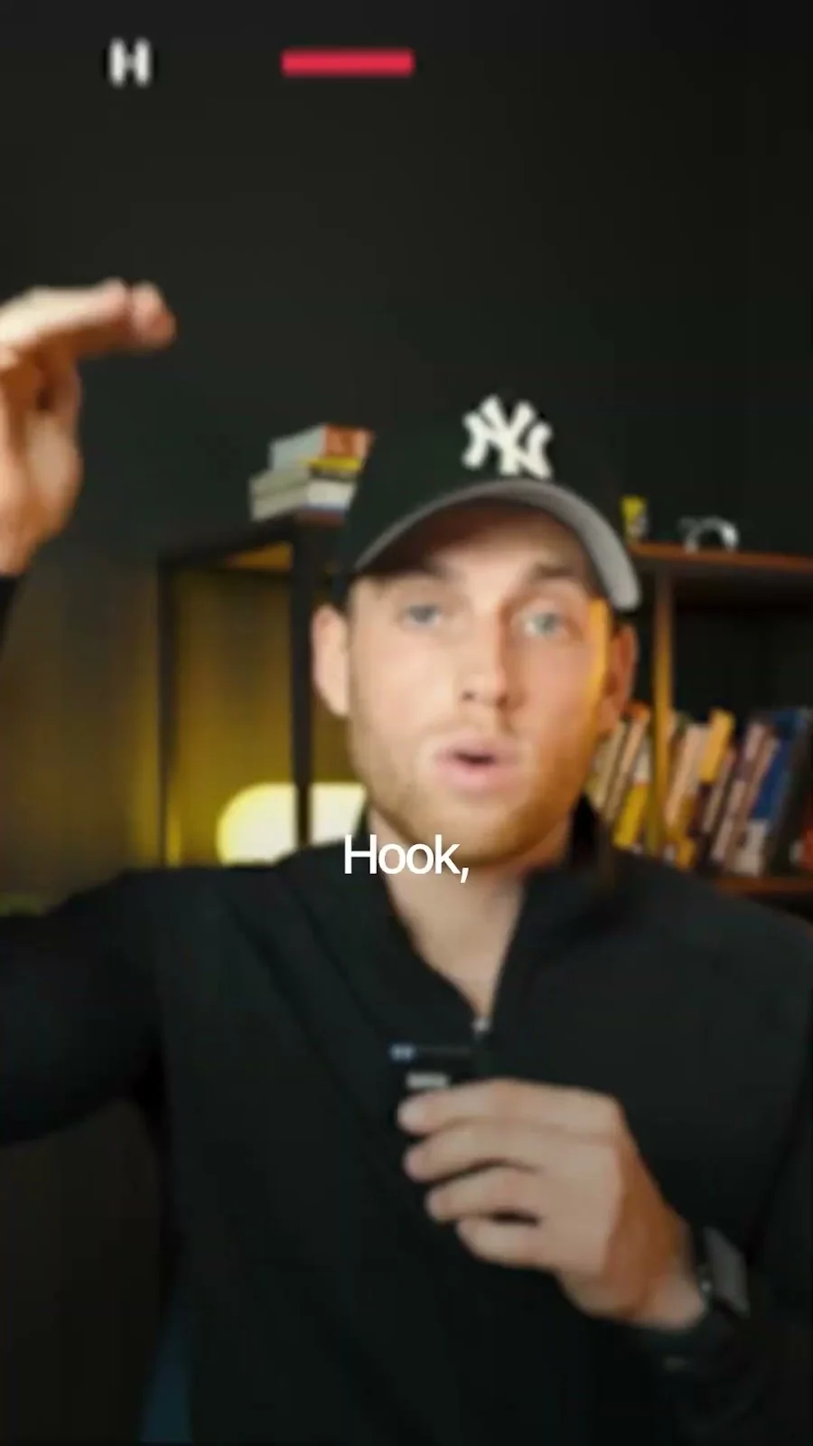 Video frame of a man in a Yankees cap talking to camera beside a bookshelf, with the caption “Hook,”